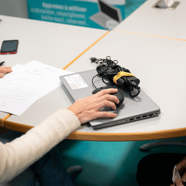 Remise d’un kit informatique reconditionné à un étudiant : un ordinateur portable, sa souris et son chargeur sont posés sur la table tandis qu’une personne signe les documents de mise à disposition.