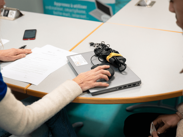 Remise d’un kit informatique reconditionné à un étudiant : un ordinateur portable, sa souris et son chargeur sont posés sur la table tandis qu’une personne signe les documents de mise à disposition.